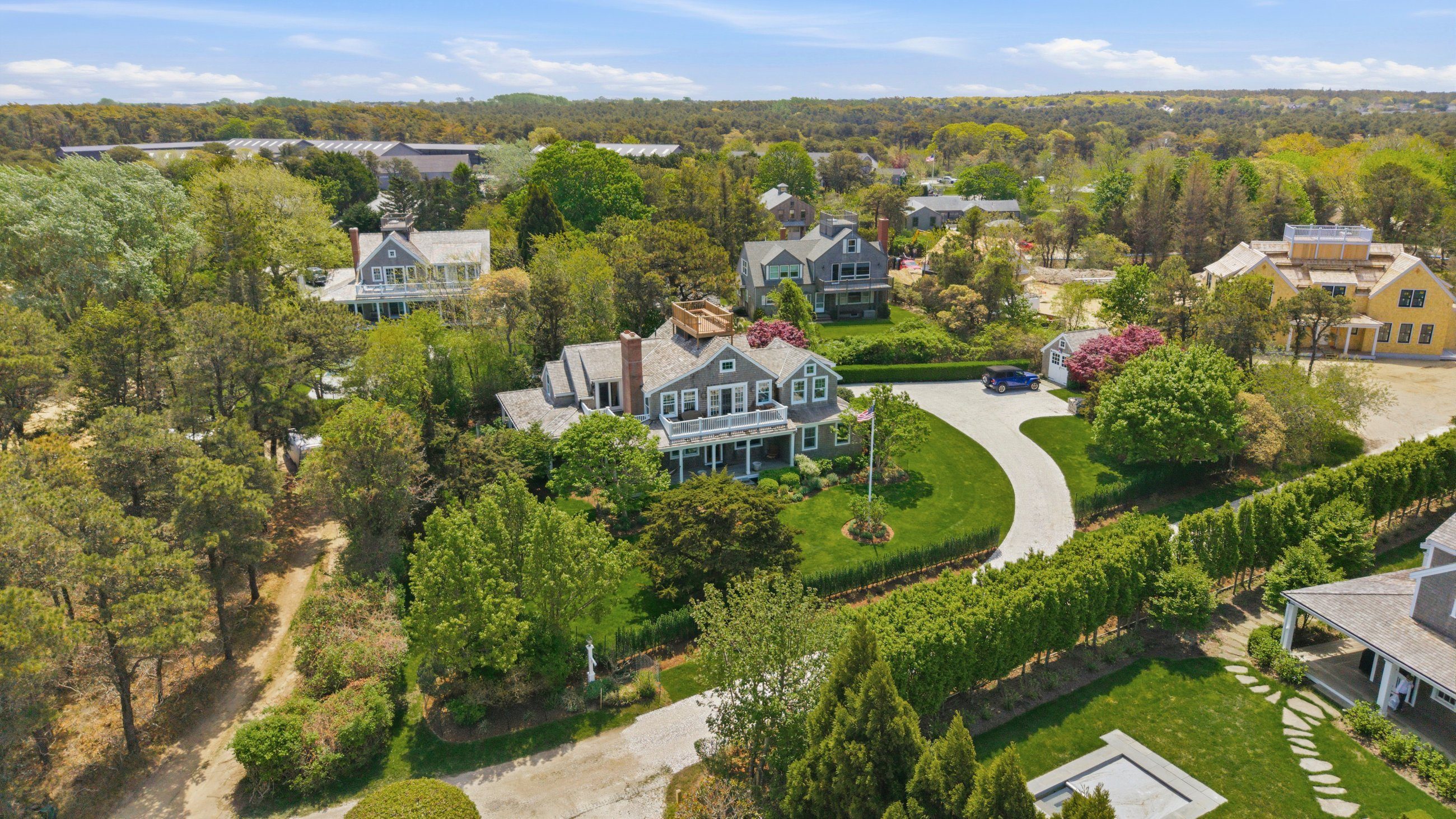 Aerial view of a gray-shingled home with landscaped grounds and a curved driveway.