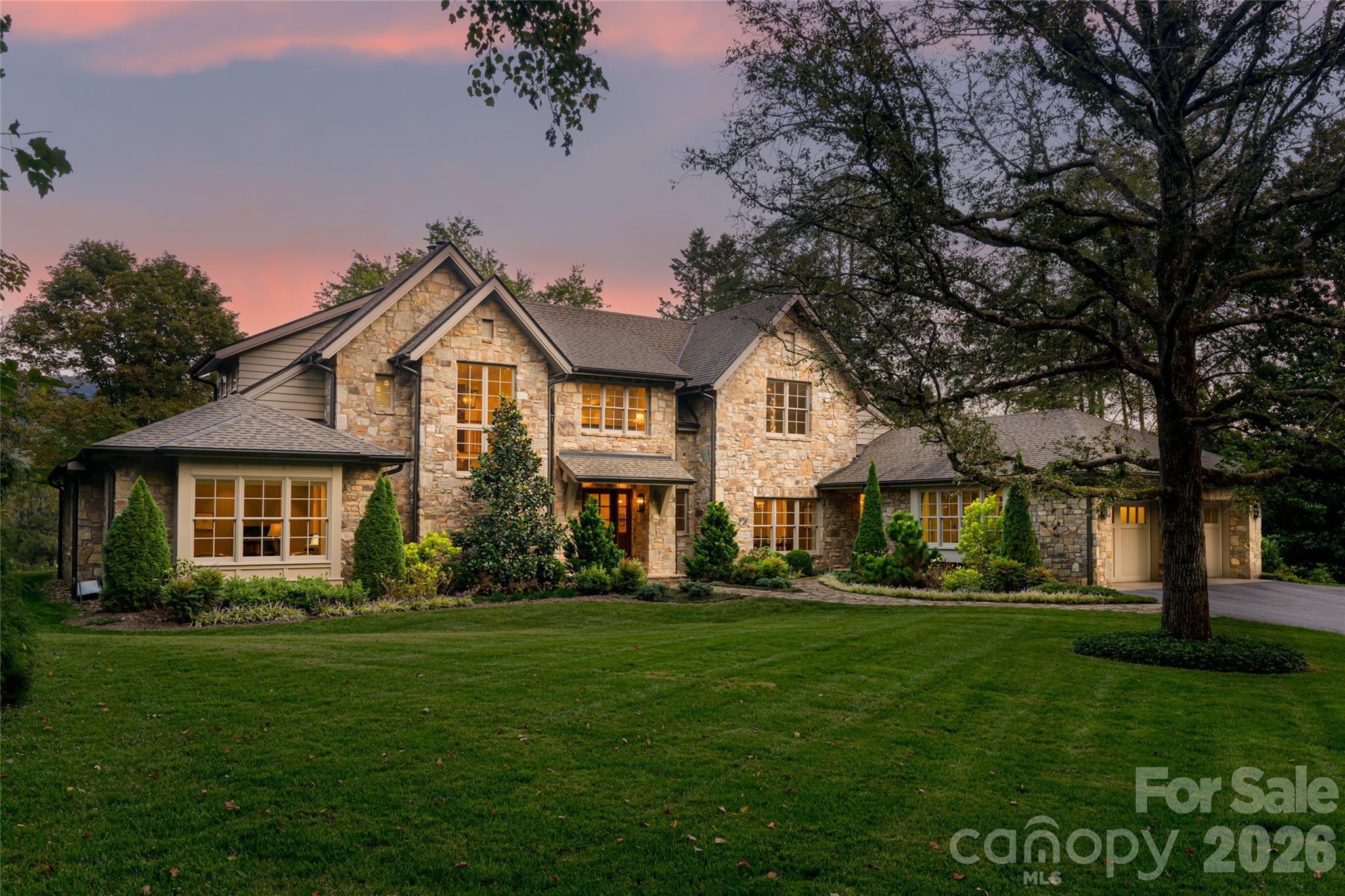 Stone-and-siding home with illuminated windows beneath a pink dusk sky.