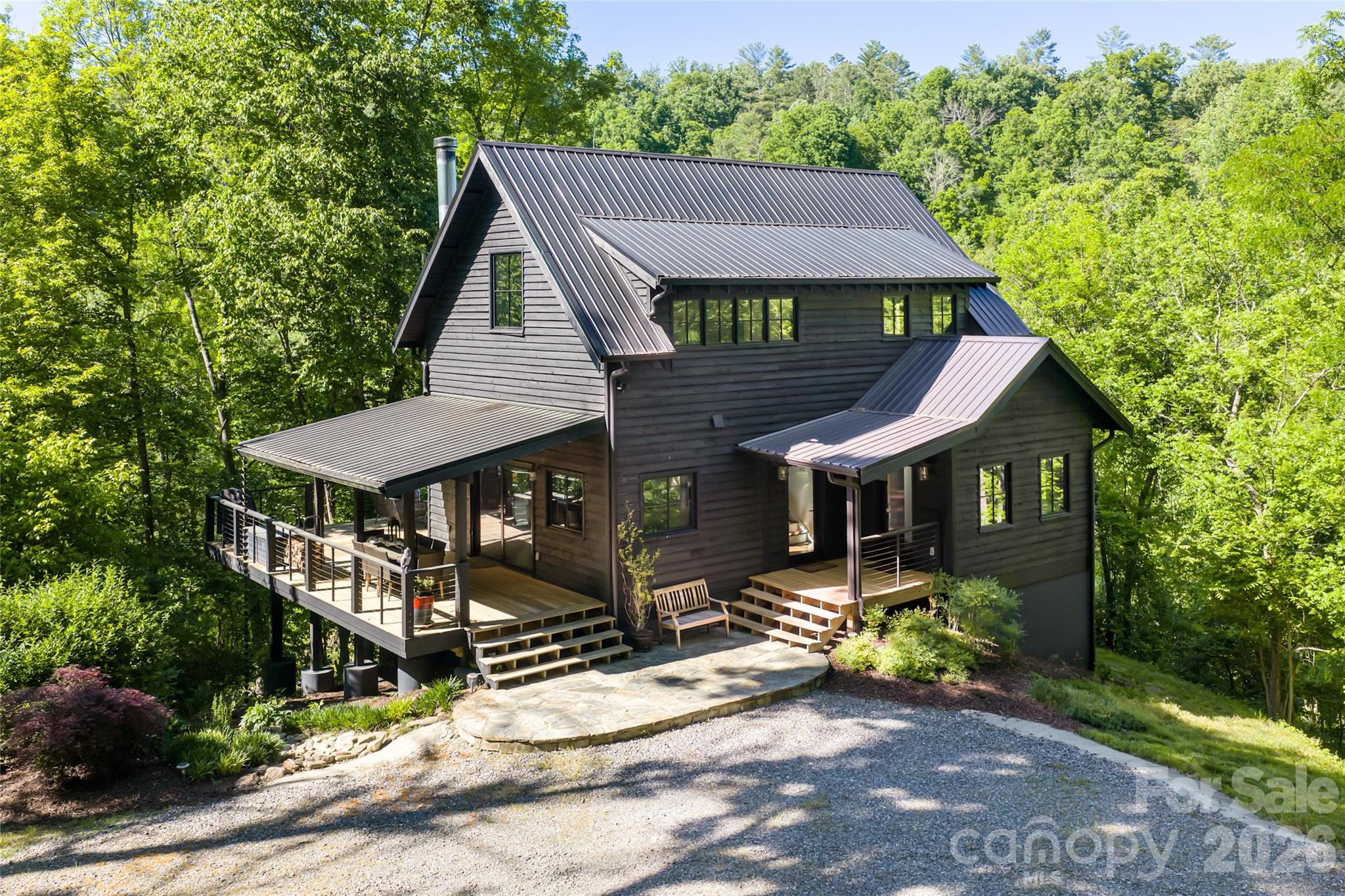 Dark gray house with a metal roof and wraparound deck surrounded by trees.
