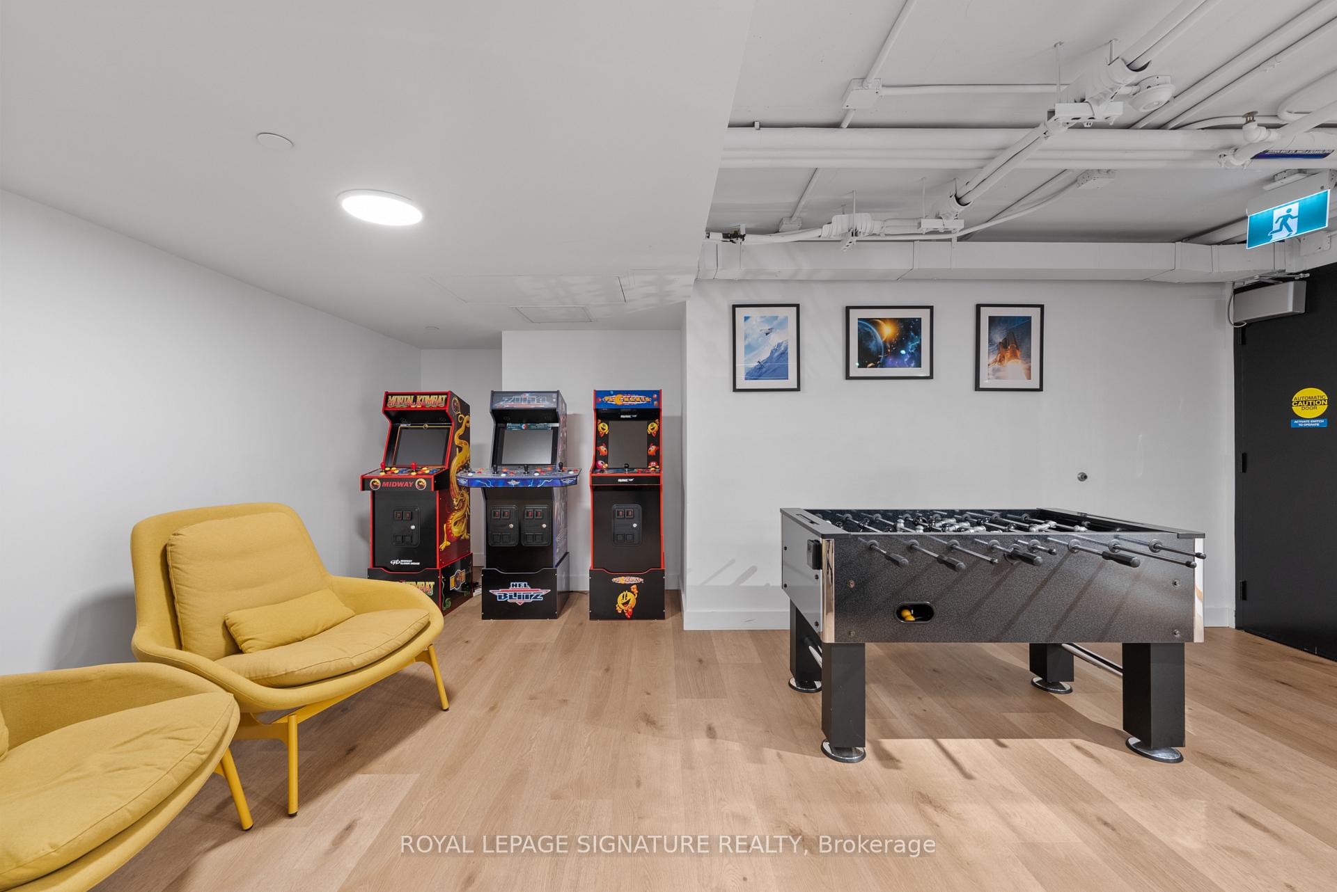 Recreation room with a foosball table, three arcade cabinets, and mustard-yellow lounge chairs.