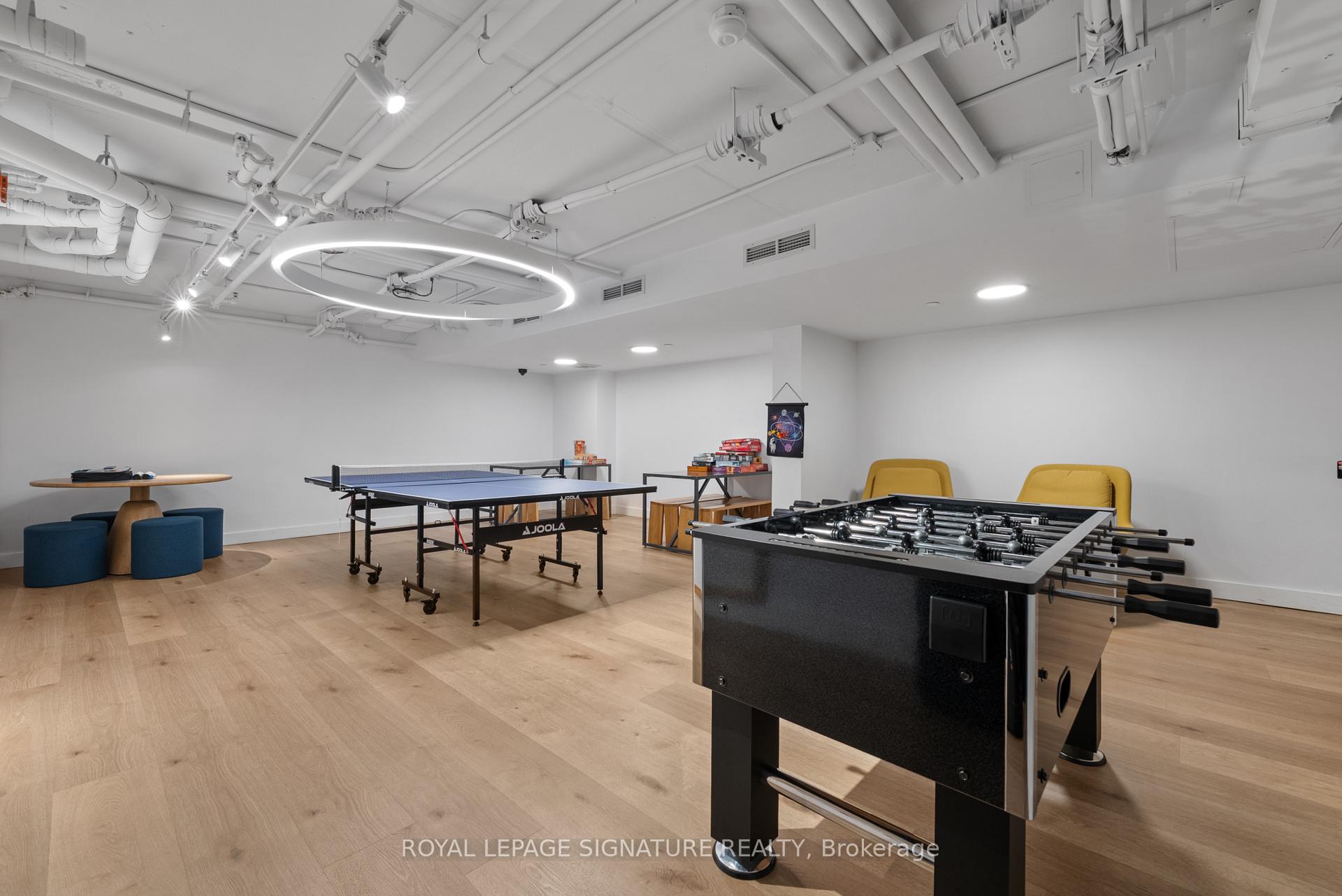 Recreation room with foosball and ping-pong tables, yellow chairs, and pale wood flooring.