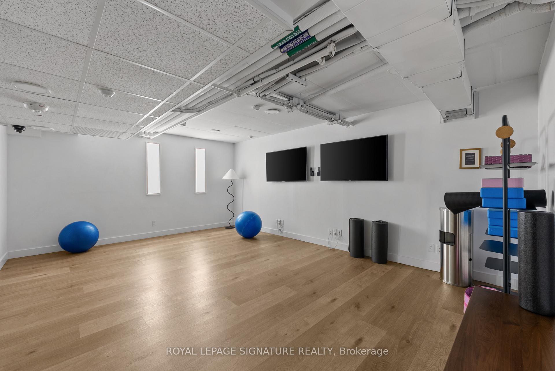 Fitness room with wood flooring, wall-mounted screens, blue exercise balls, and workout equipment.