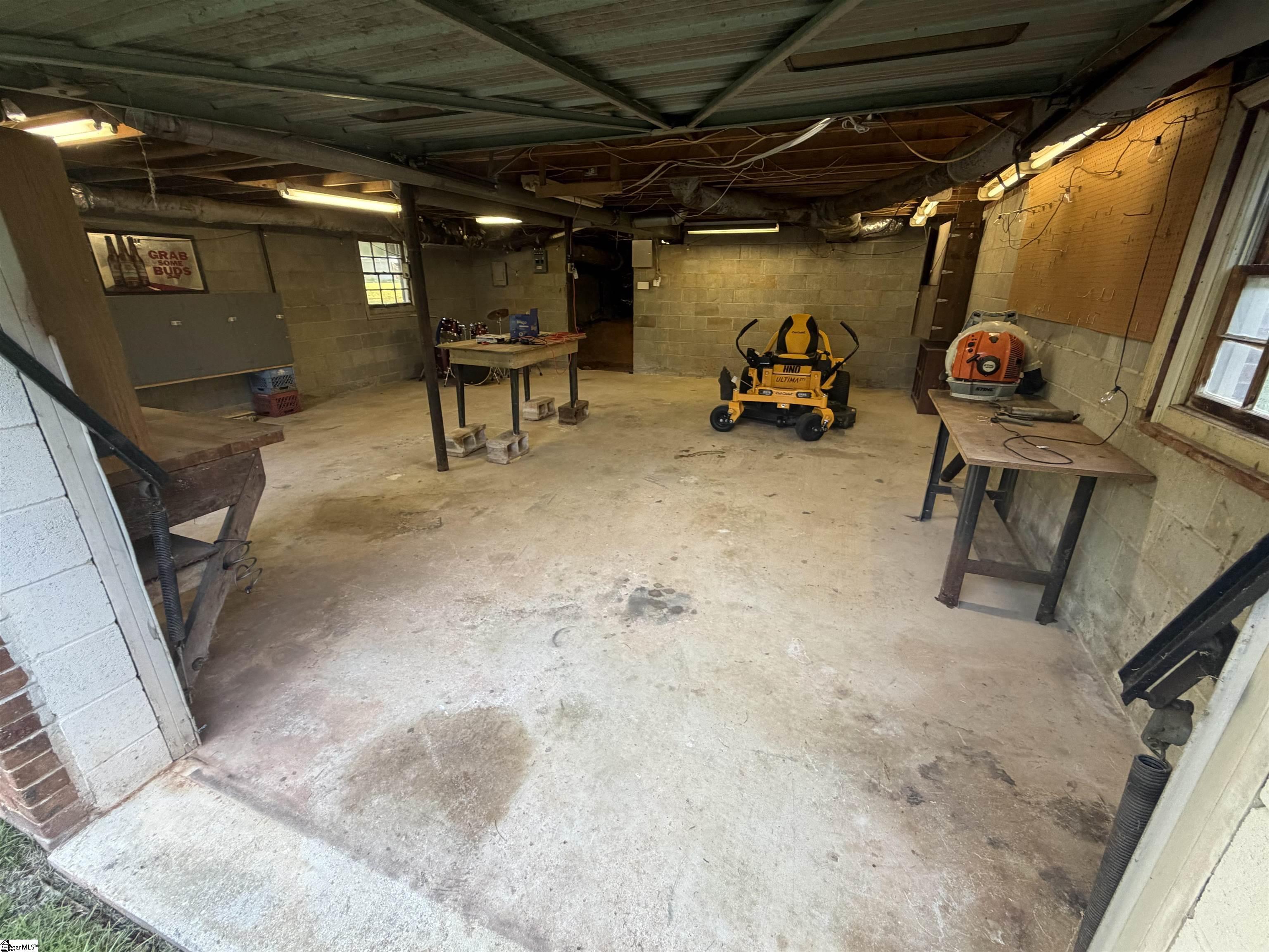 Garage workshop with concrete block walls, worktables, a yellow riding mower, and a saw.