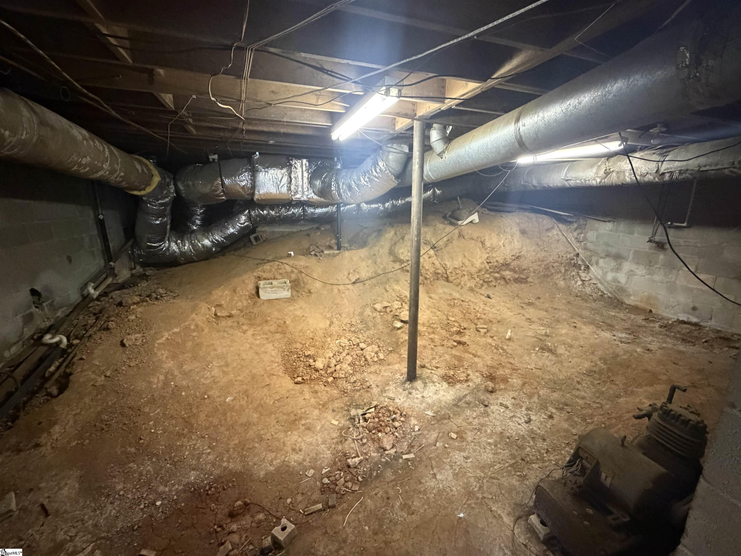 Dirt-floor crawlspace with exposed HVAC ducts, cinder-block walls, and a central support post.