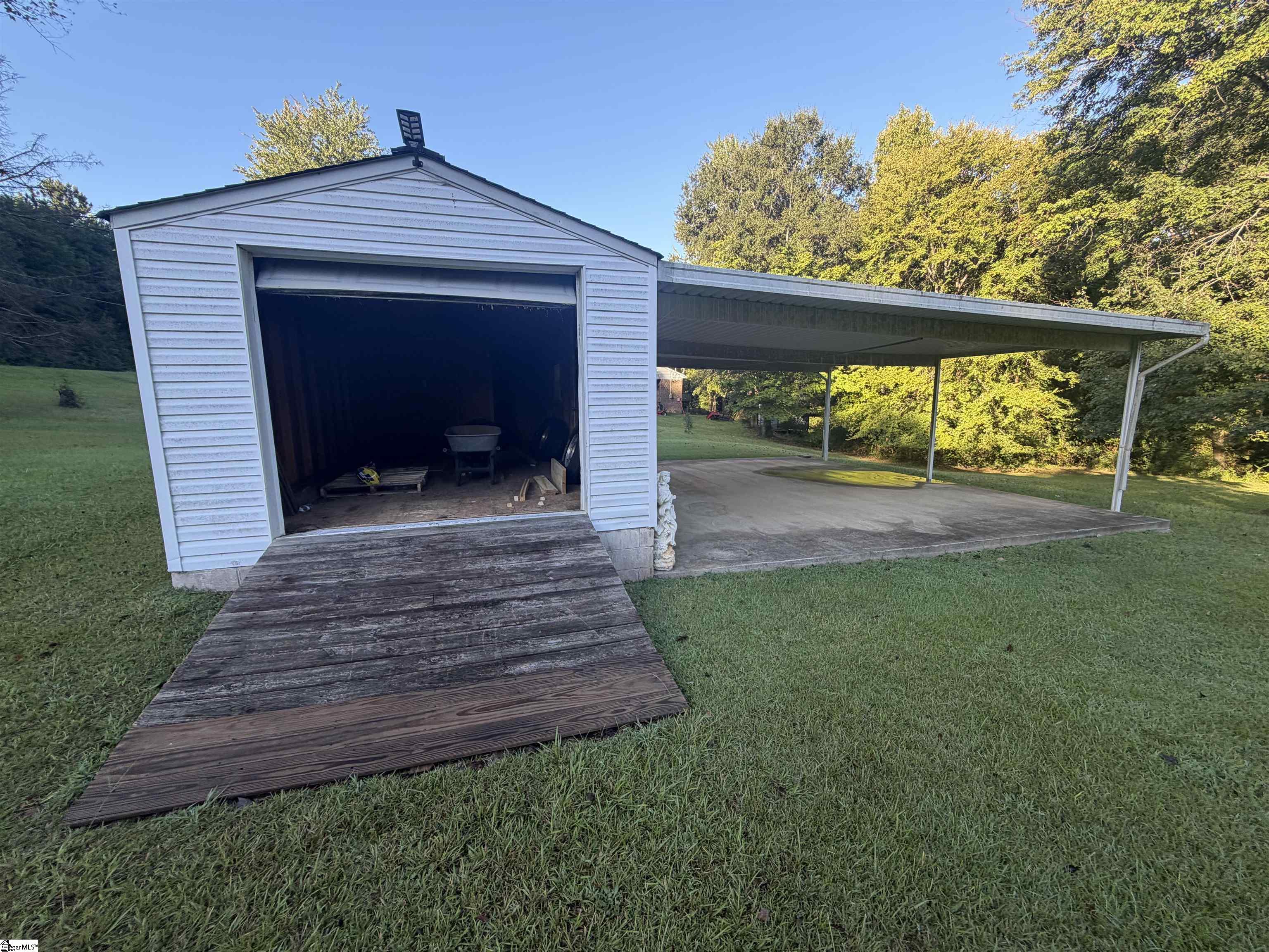 Detached white garage with an open bay, wooden ramp, and attached carport beside a grassy yard.