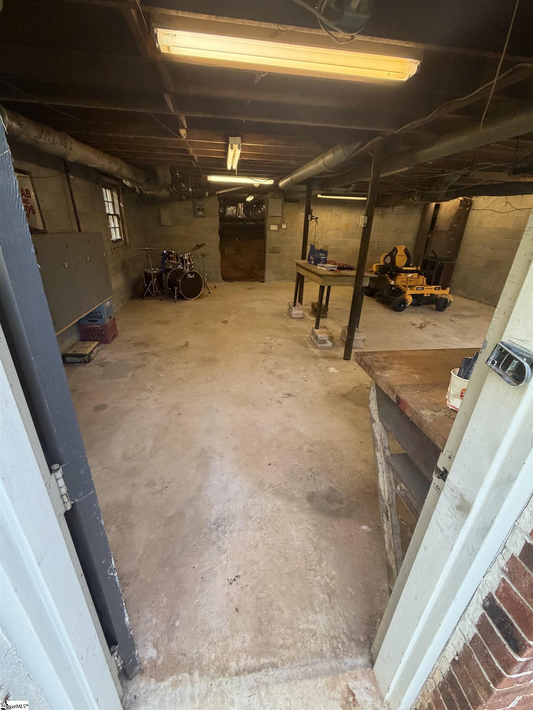 Unfinished basement workshop with a drum kit, workbench, and riding lawn mower.