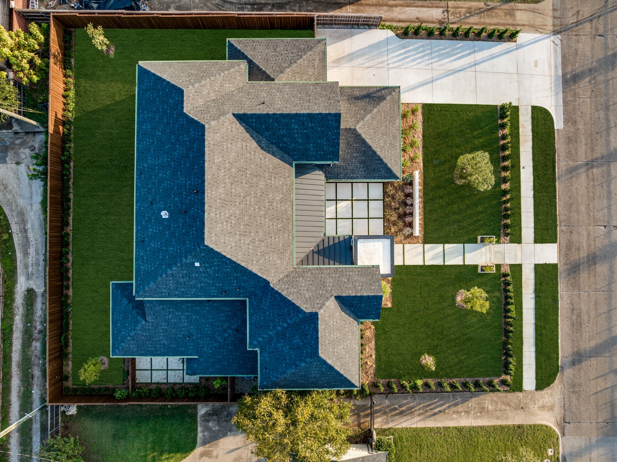 Aerial view of a home with intersecting rooflines, fenced lawn, and broad concrete driveway.