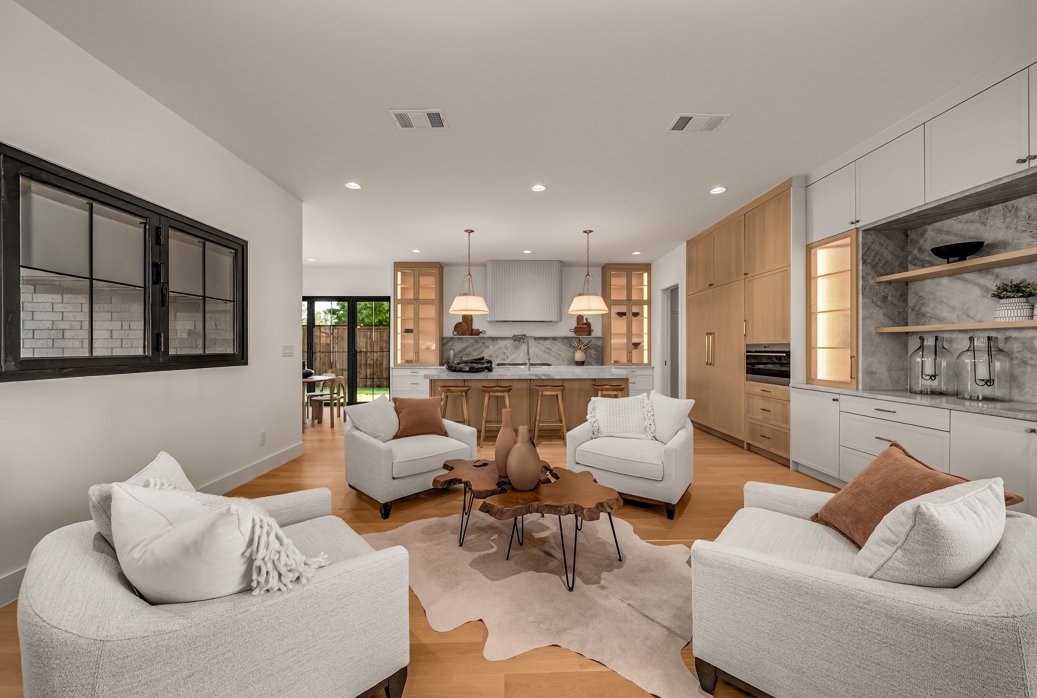 Open-plan living room and kitchen with white seating, light oak cabinets, and a marble backsplash.