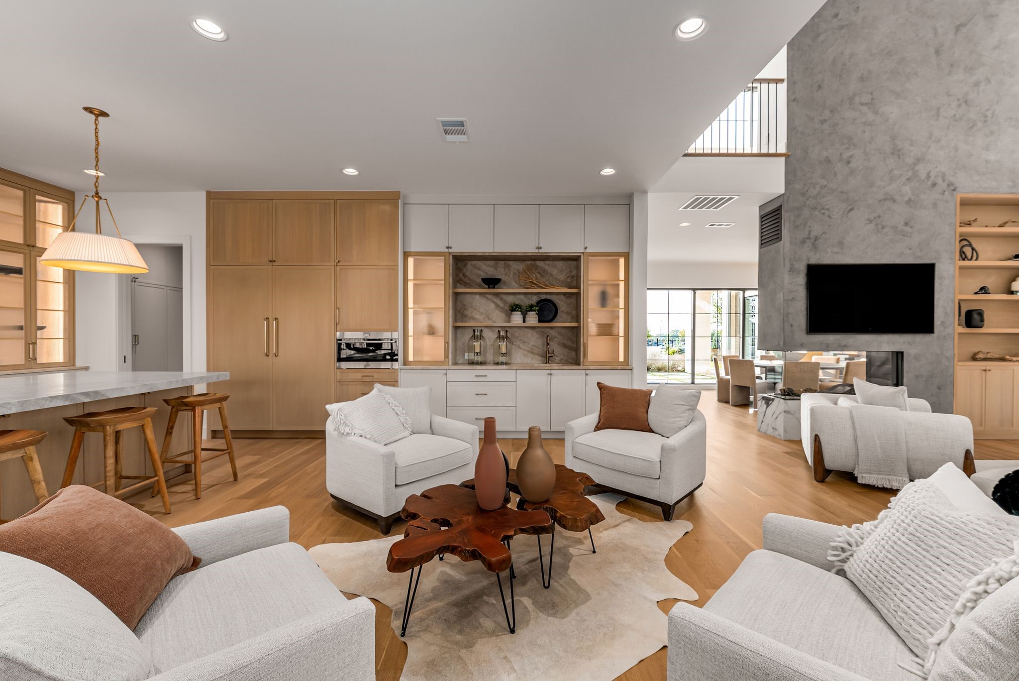 Open-plan living room with white sofas, wood cabinetry, and a stone fireplace wall.