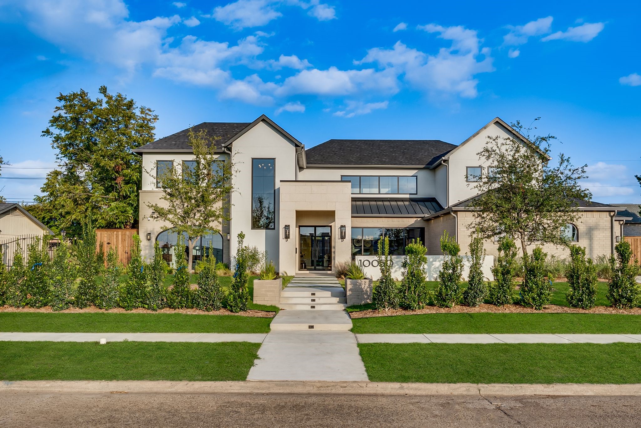 Modern two-story home with cream and white exterior, dark gabled roofs, and landscaped front entry.