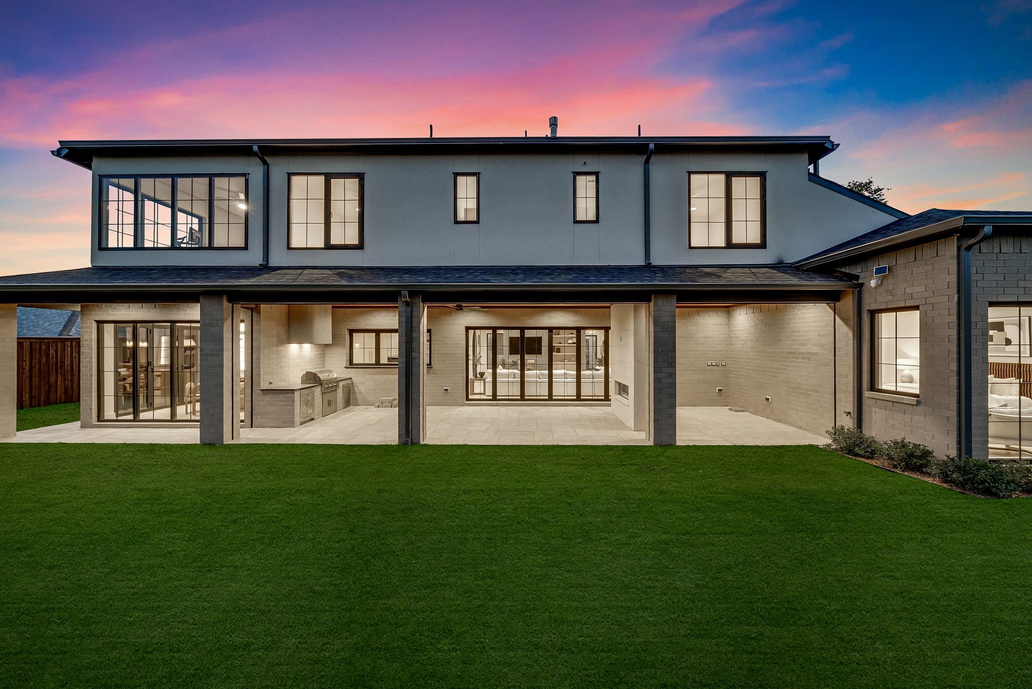 Modern two-story home with a broad covered patio and outdoor kitchen at dusk.