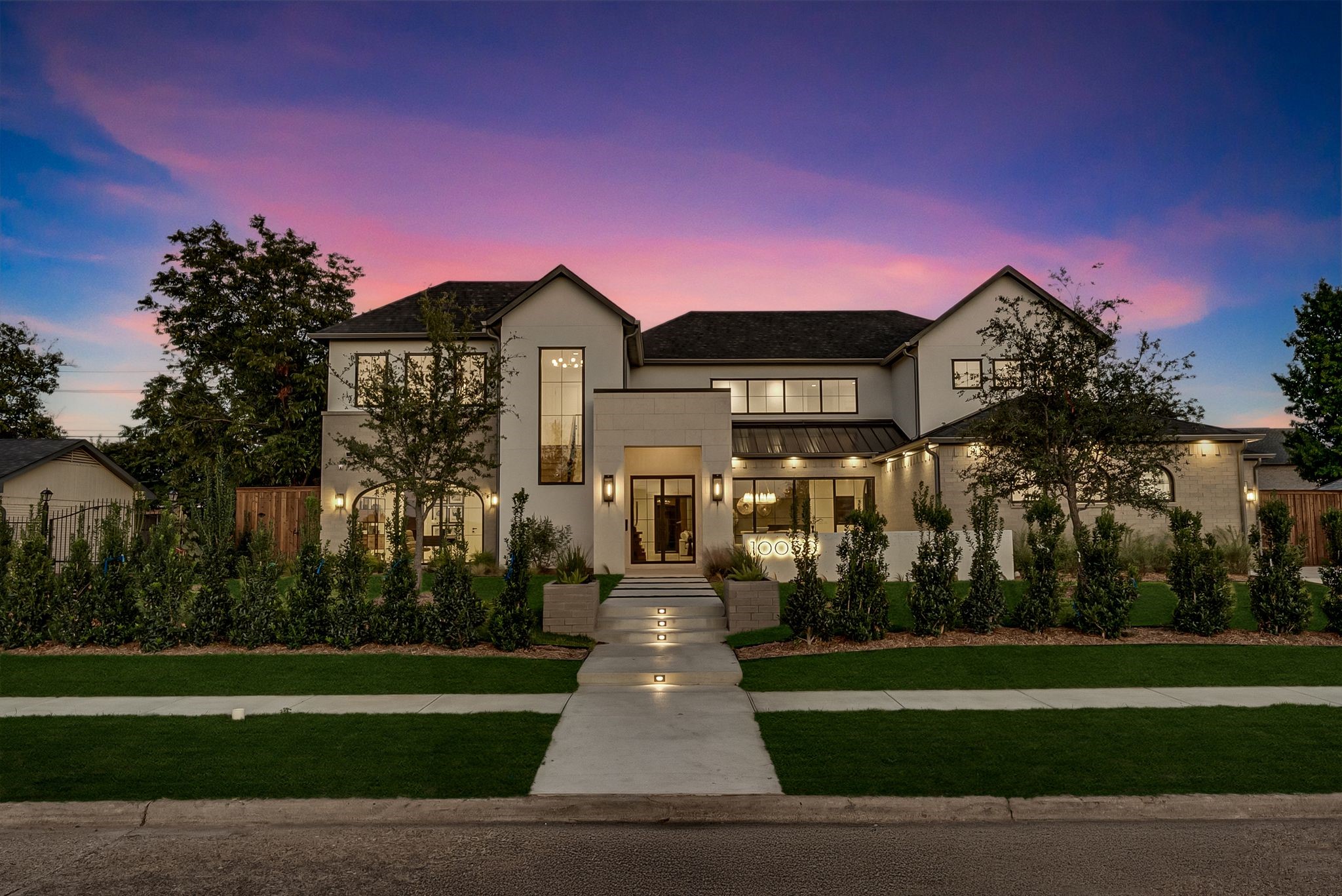 Modern two-story home at dusk with landscaped grounds and an illuminated walkway to the entrance.
