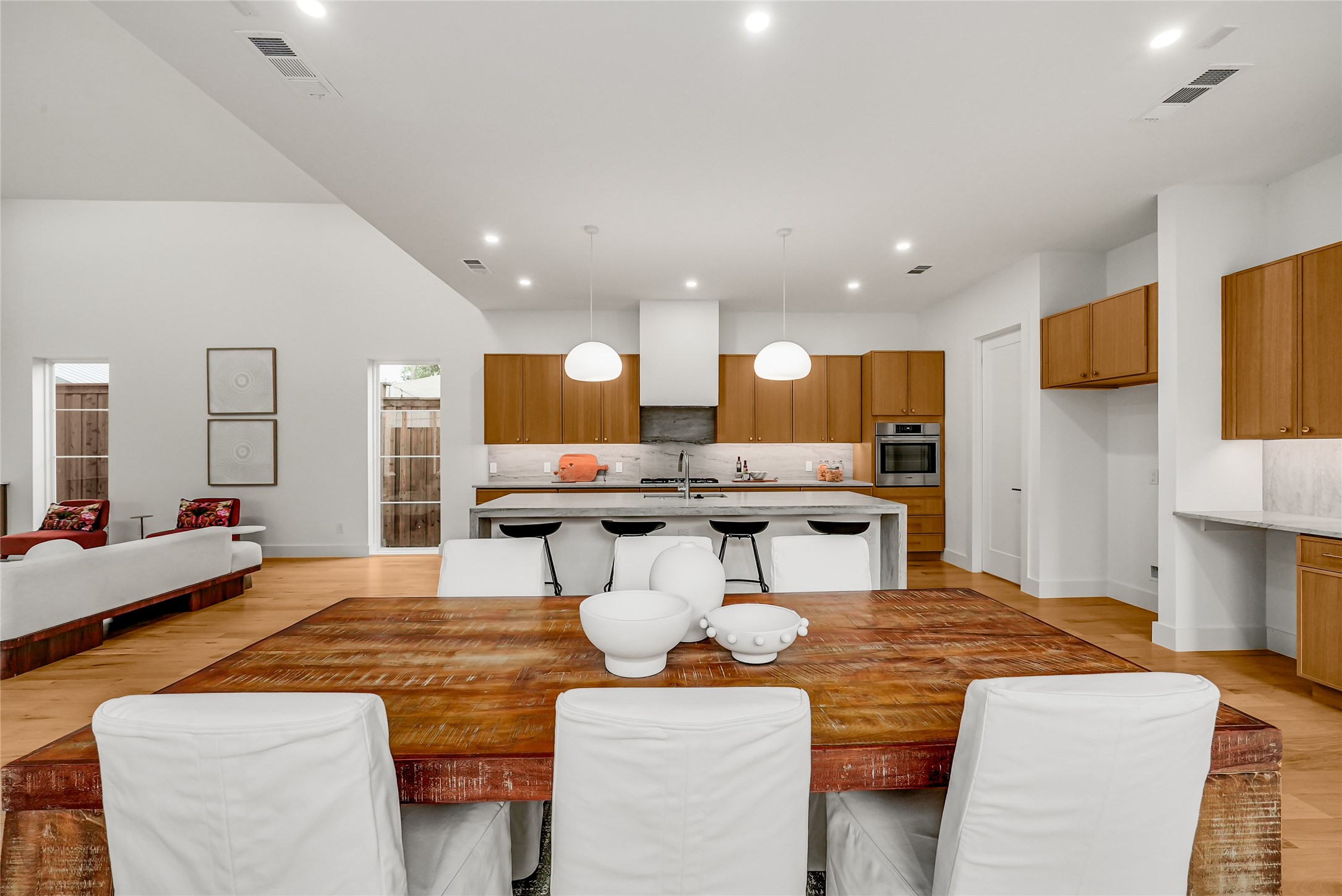 Open-plan kitchen with wood cabinetry, marble island, and a rustic dining table with white chairs.