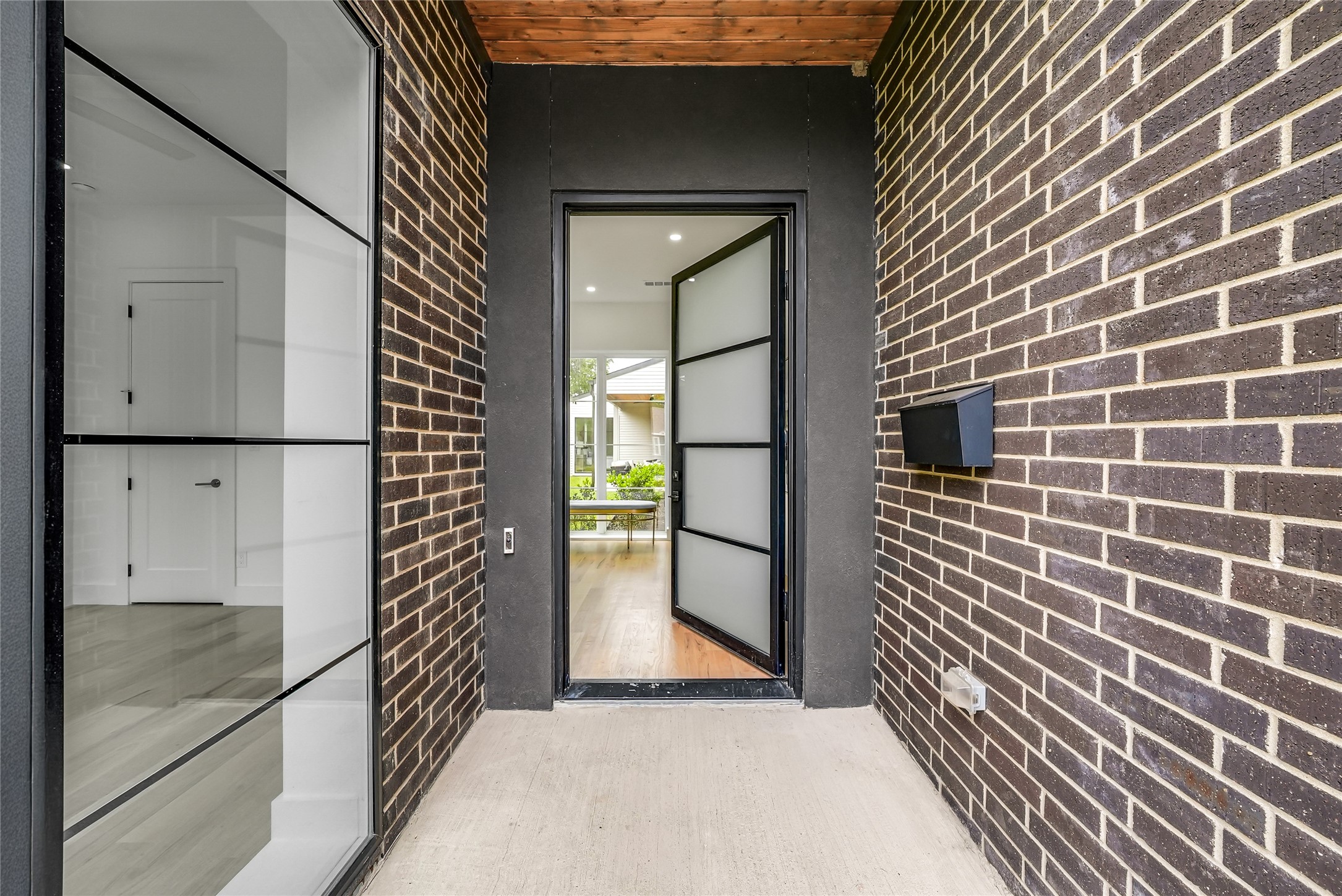 Covered brick entry with a wood ceiling and an open frosted-glass front door.