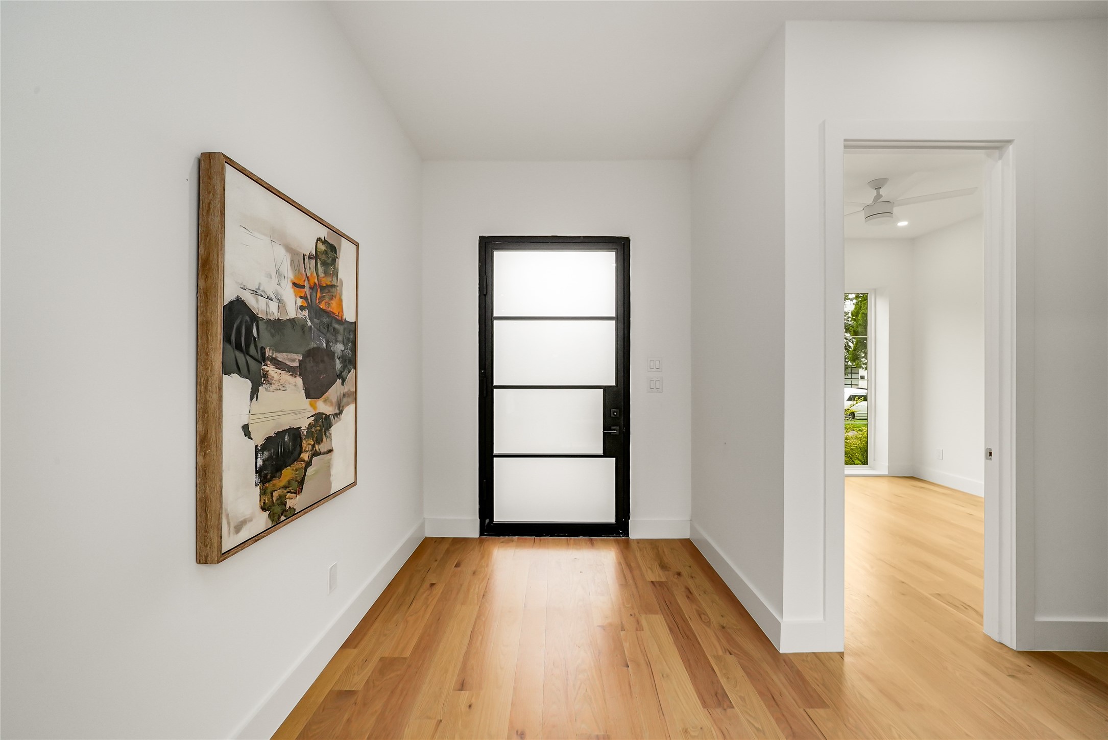 Entry hall with warm hardwood floors, abstract wall art, and a black-framed frosted-glass door.