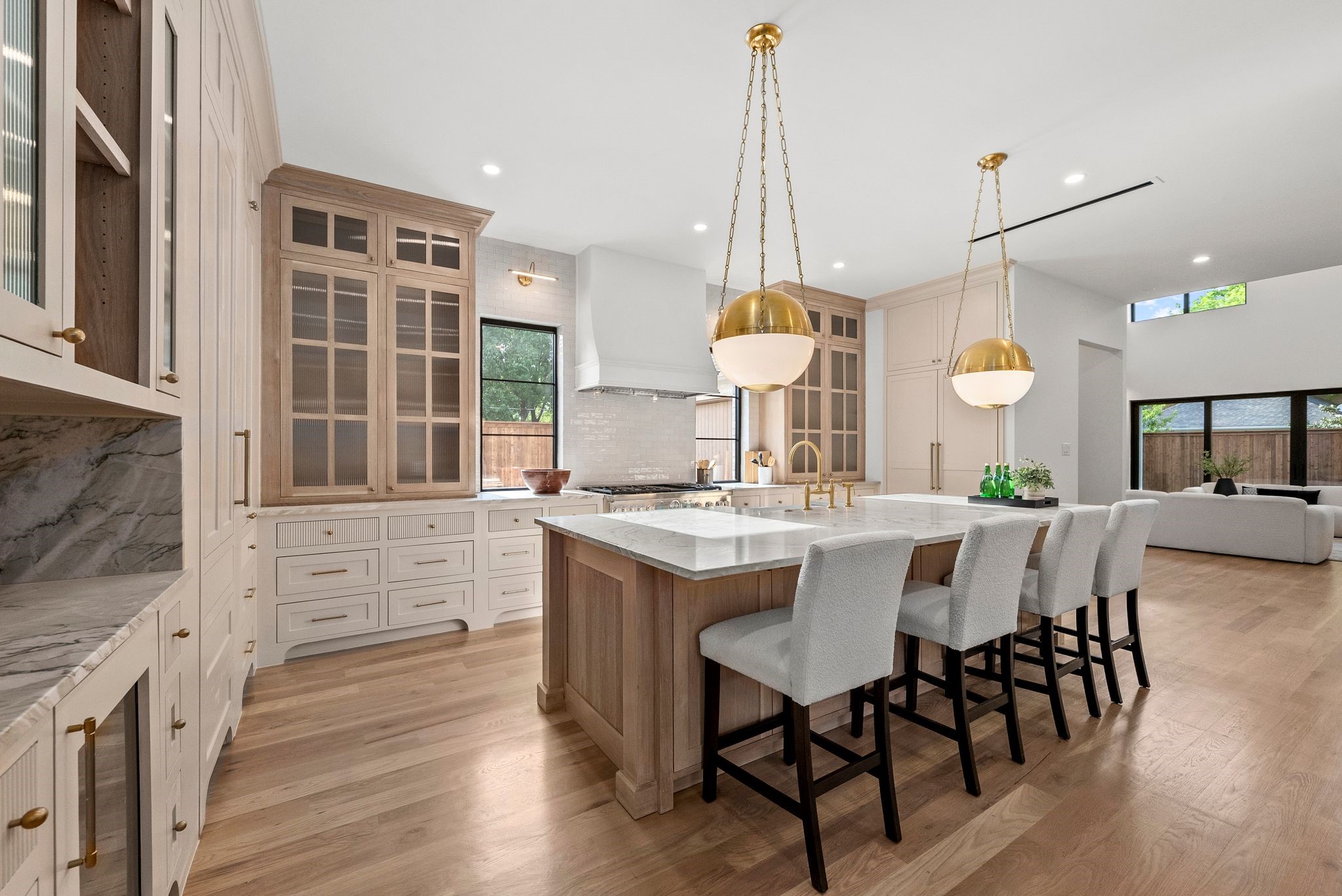 Bright kitchen with a large marble island, cream cabinetry, brass pendants, and hardwood floors.