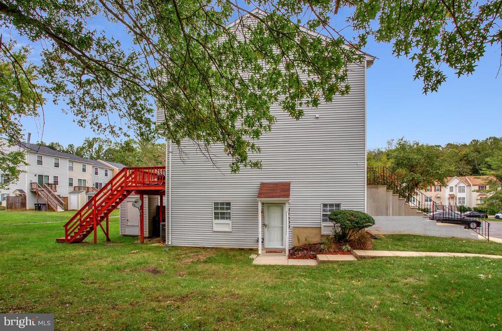 Townhouse rear exterior with red stairs, a white entry door, and a lawn beneath leafy trees.