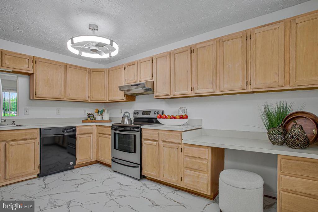 Kitchen with light wood cabinetry, stainless steel appliances, and white marble-look flooring.
