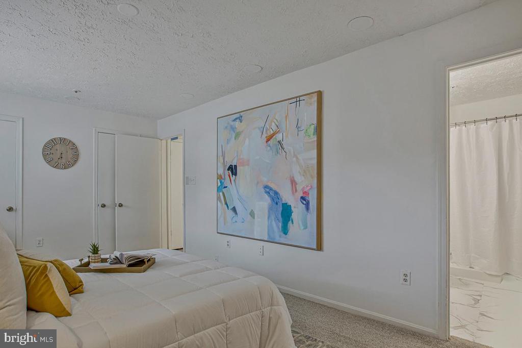 Furnished bedroom with a white bed, mustard-yellow pillows, and colorful abstract wall art.