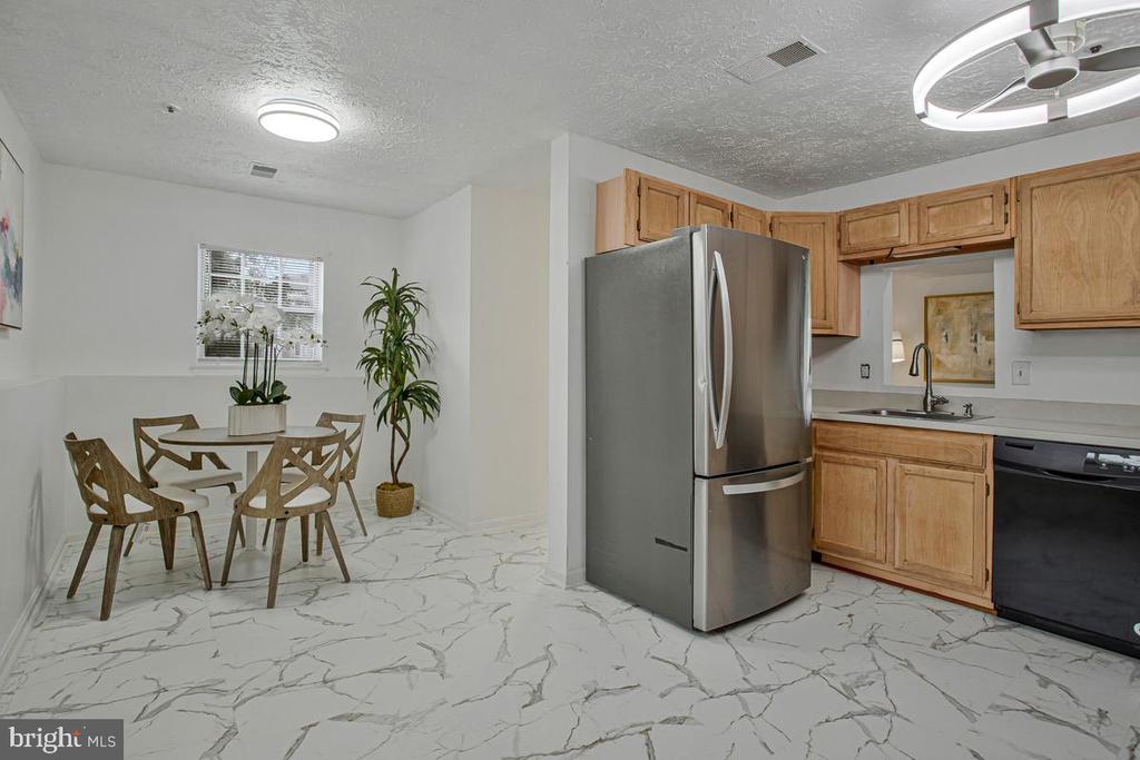 Kitchen and dining area with wood cabinets, a stainless steel refrigerator, and veined flooring.