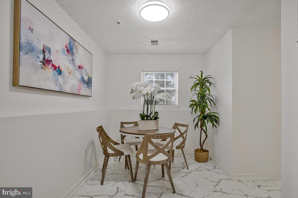 Dining room with a round table, orchid centerpiece, tall plant, and marble-patterned floor.