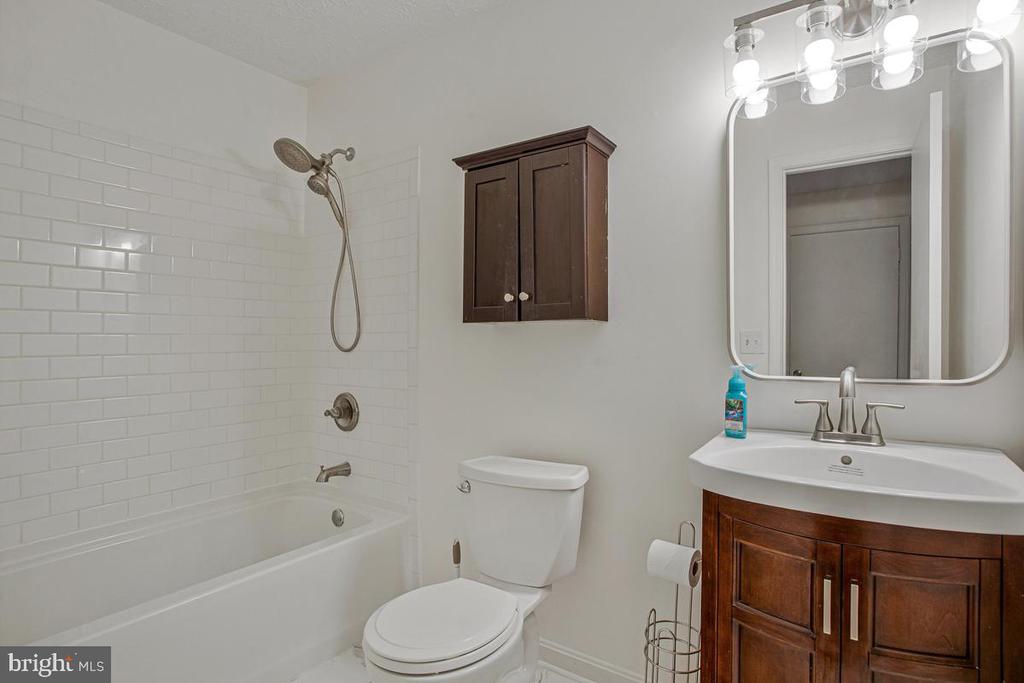 Bathroom with a white tiled tub-shower, dark wood vanity, and large mirror.