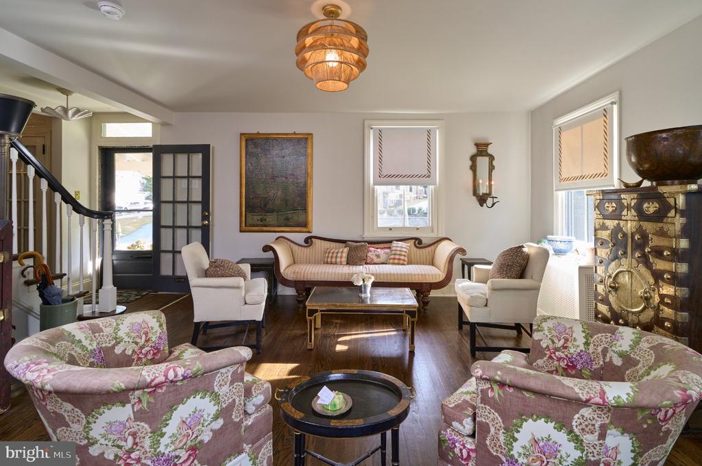 Furnished living room with floral armchairs, a carved settee, and a staircase beside the front door.