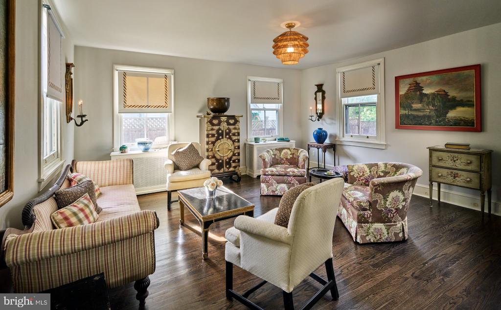 Furnished living room with patterned seating, dark hardwood floors, and several shaded windows.