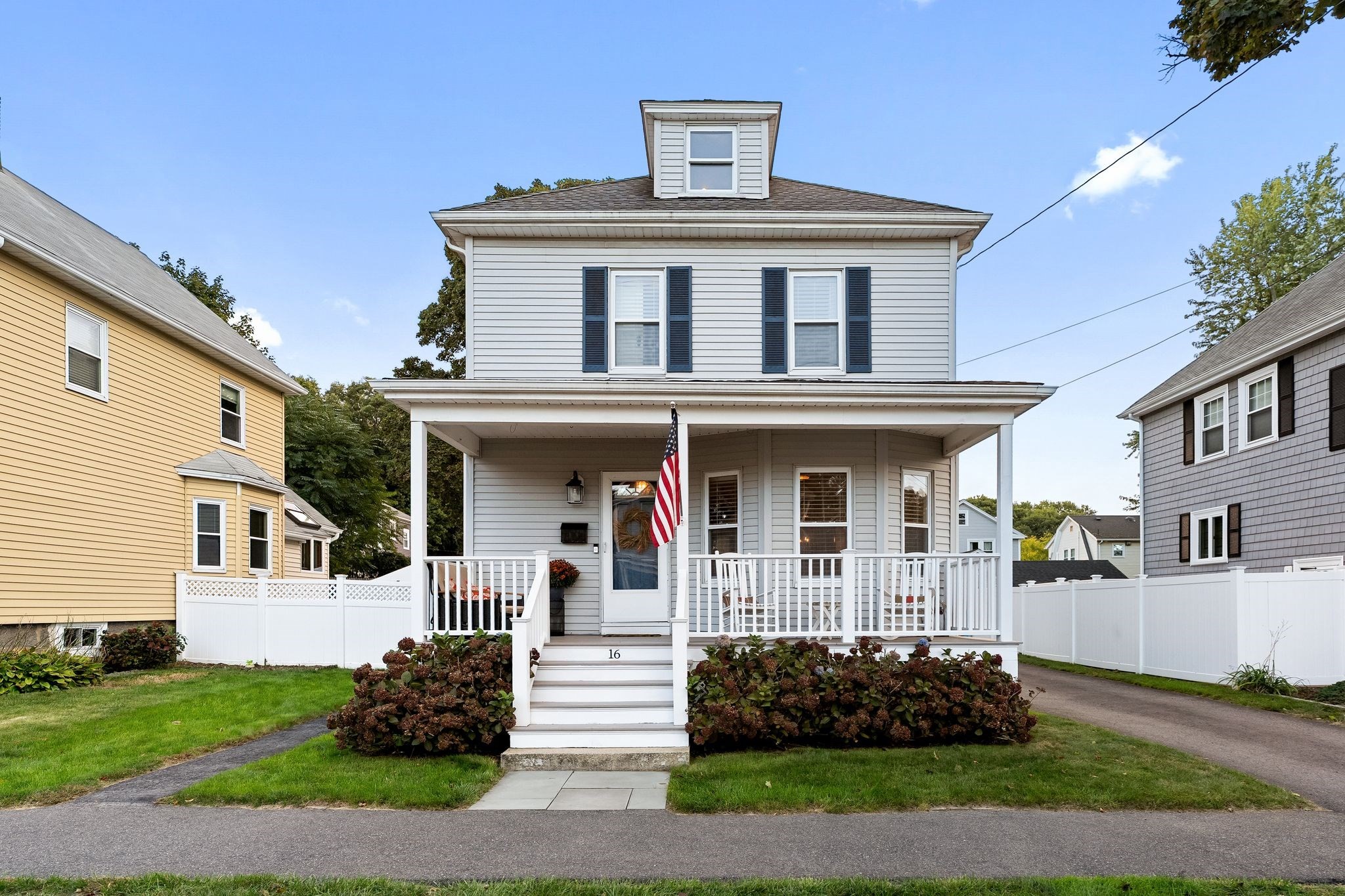 White two-story house with a covered porch, navy shutters, and an American flag by the entrance.