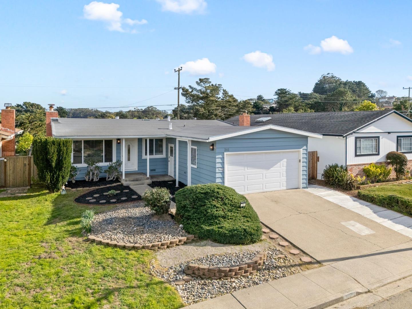 Blue single-story home with a white garage and landscaped front yard.
