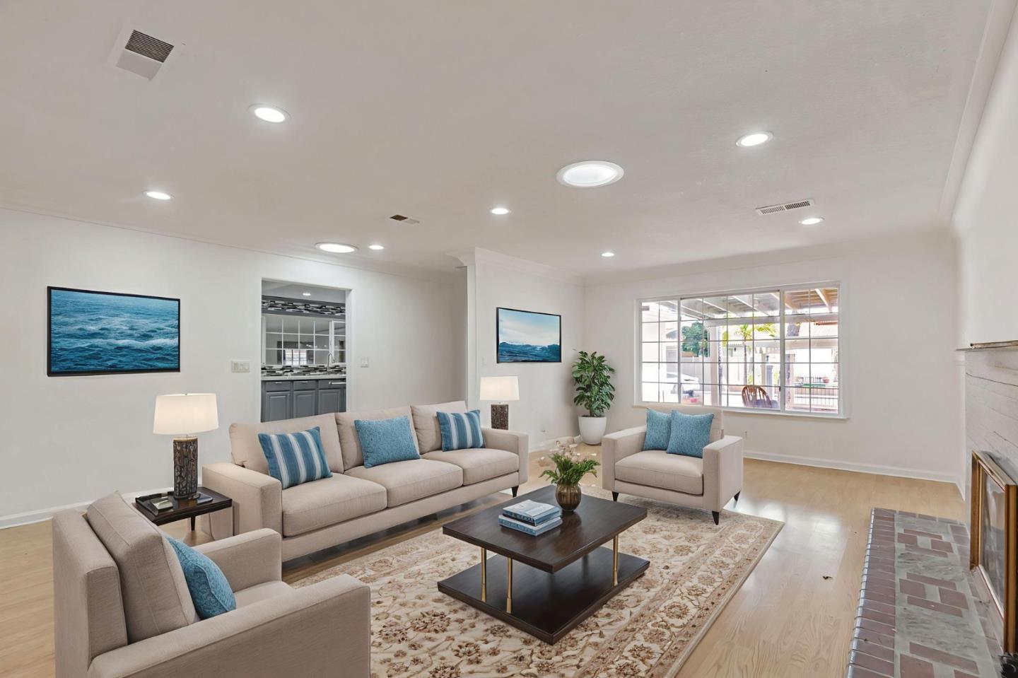 Staged living room with blue accent pillows, a patterned rug, and a large window overlooking a patio.
