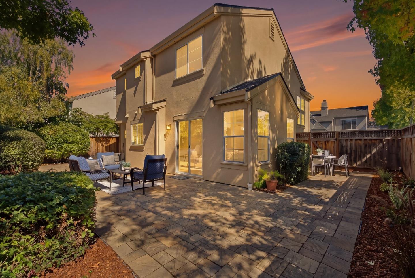 Two-story stucco home with a paved patio and outdoor seating at dusk.