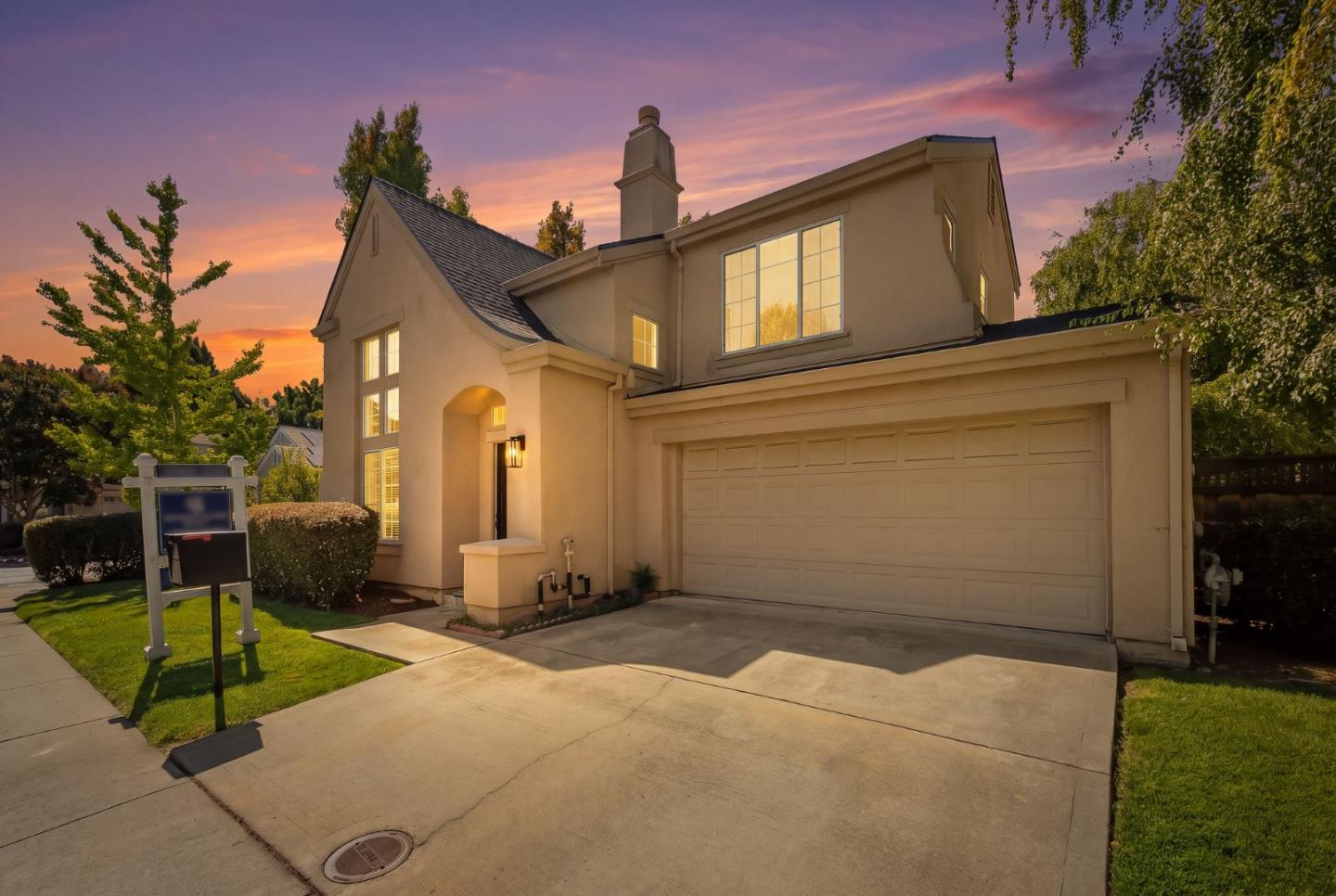 Two-story stucco house with an attached double garage and front lawn at sunset.