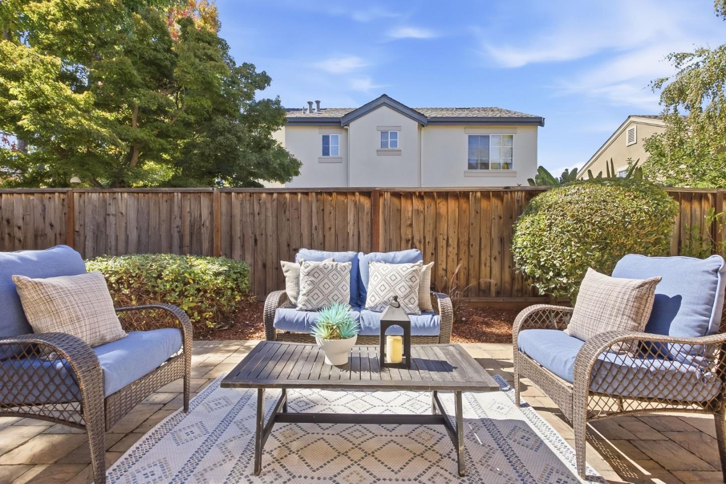 Furnished backyard patio with wicker seating, a low table, patterned rug, and tall wooden privacy fence.