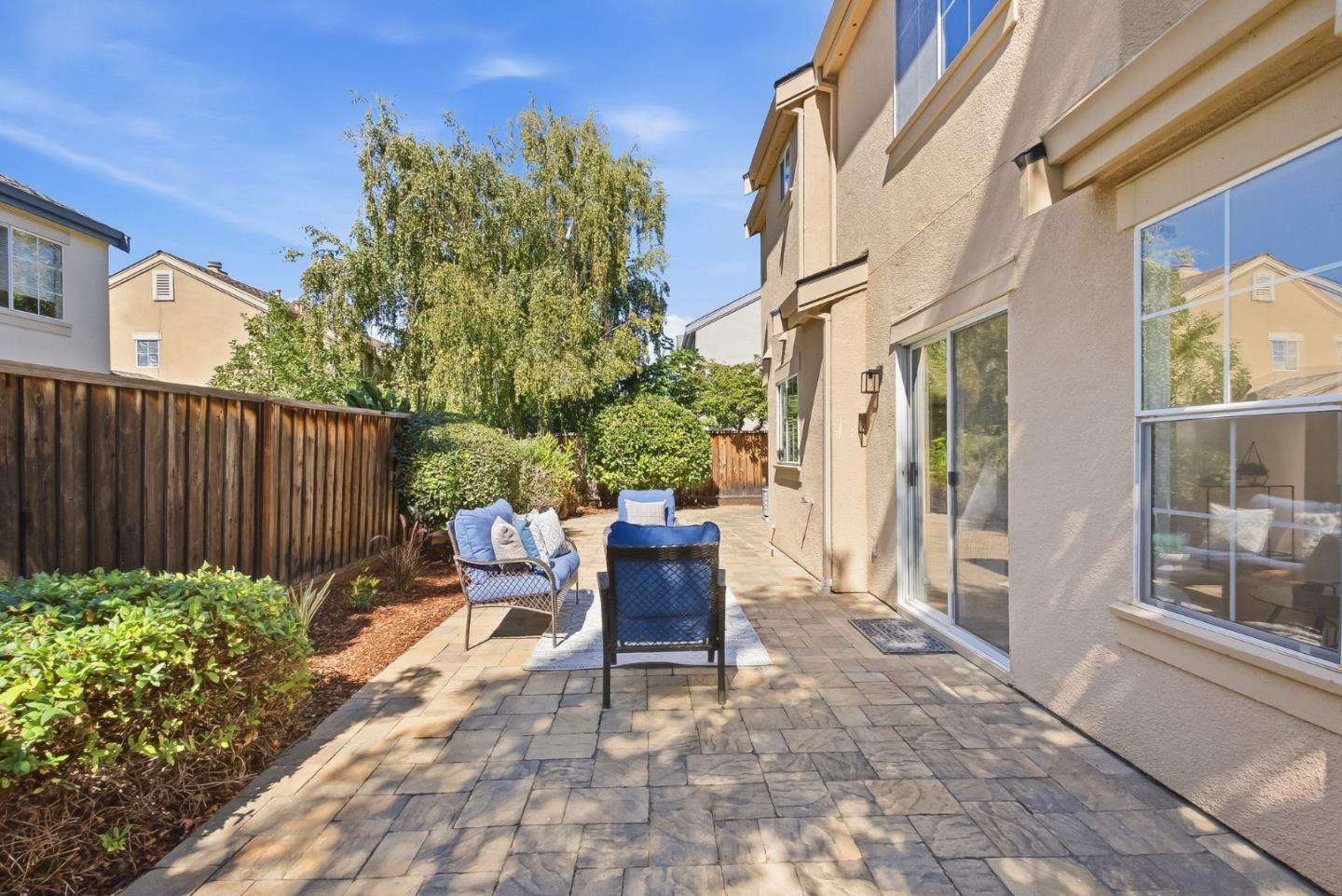 Paved backyard patio with blue-cushioned seating beside sliding glass doors.