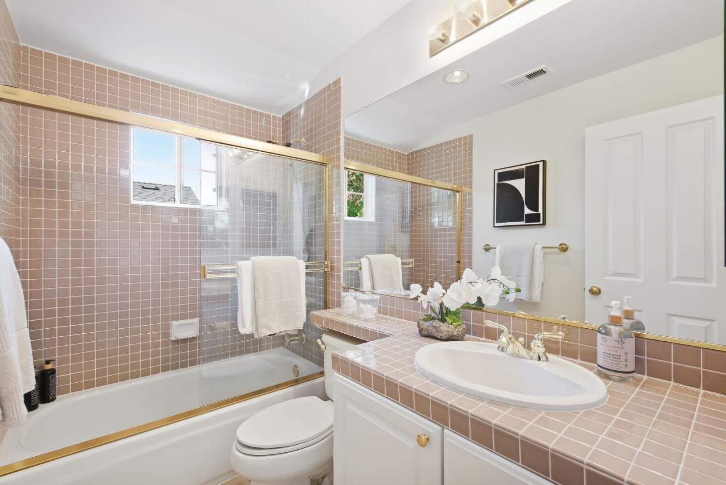 Bathroom with mauve tile, a glass-enclosed tub and shower, and a white vanity sink.