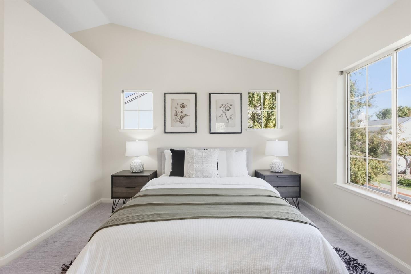 Staged bedroom with a vaulted ceiling, large windows, and a king-size bed with a sage-green throw.