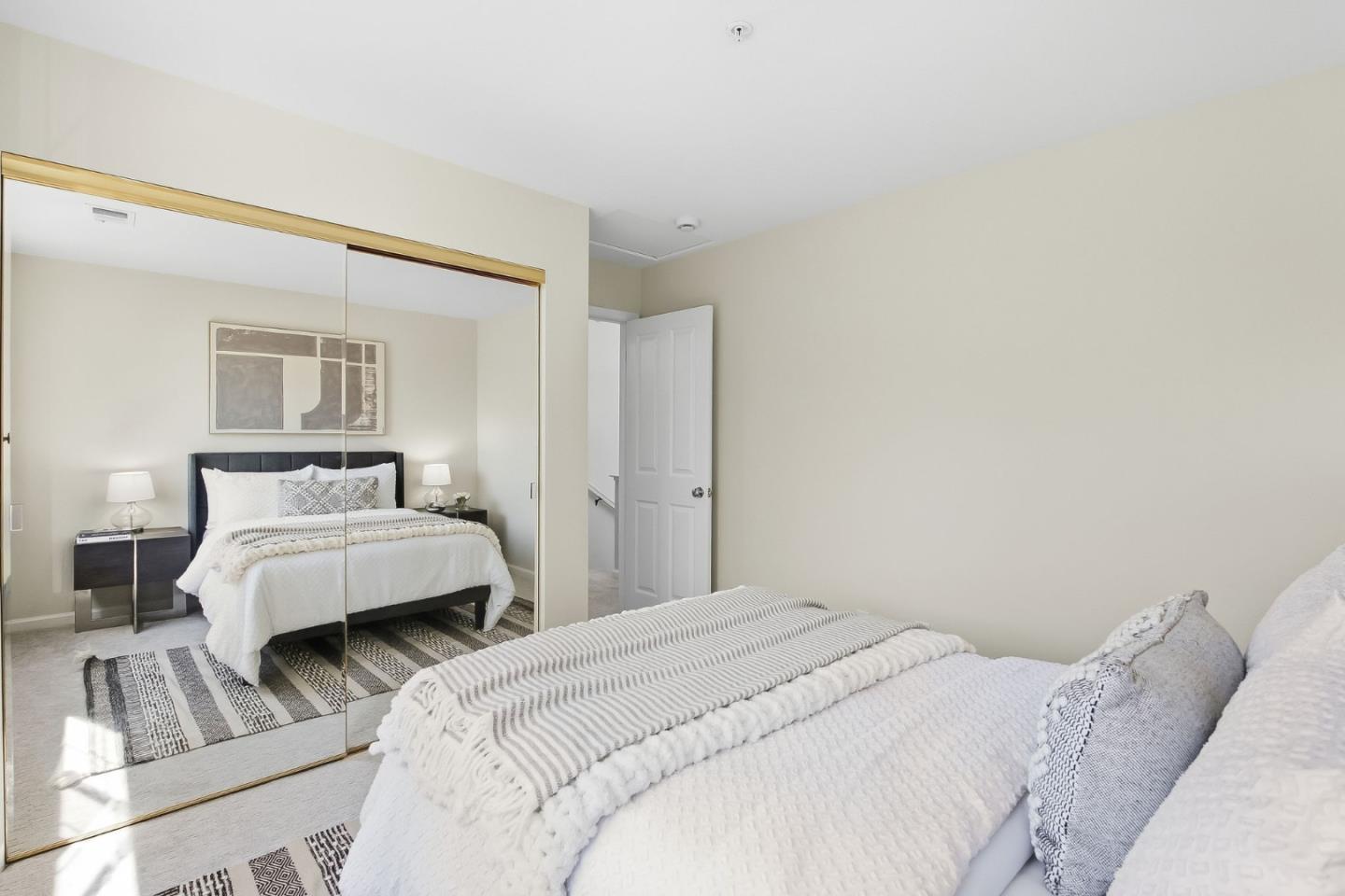Staged bedroom with a white bed, mirrored closet doors, and a striped rug.