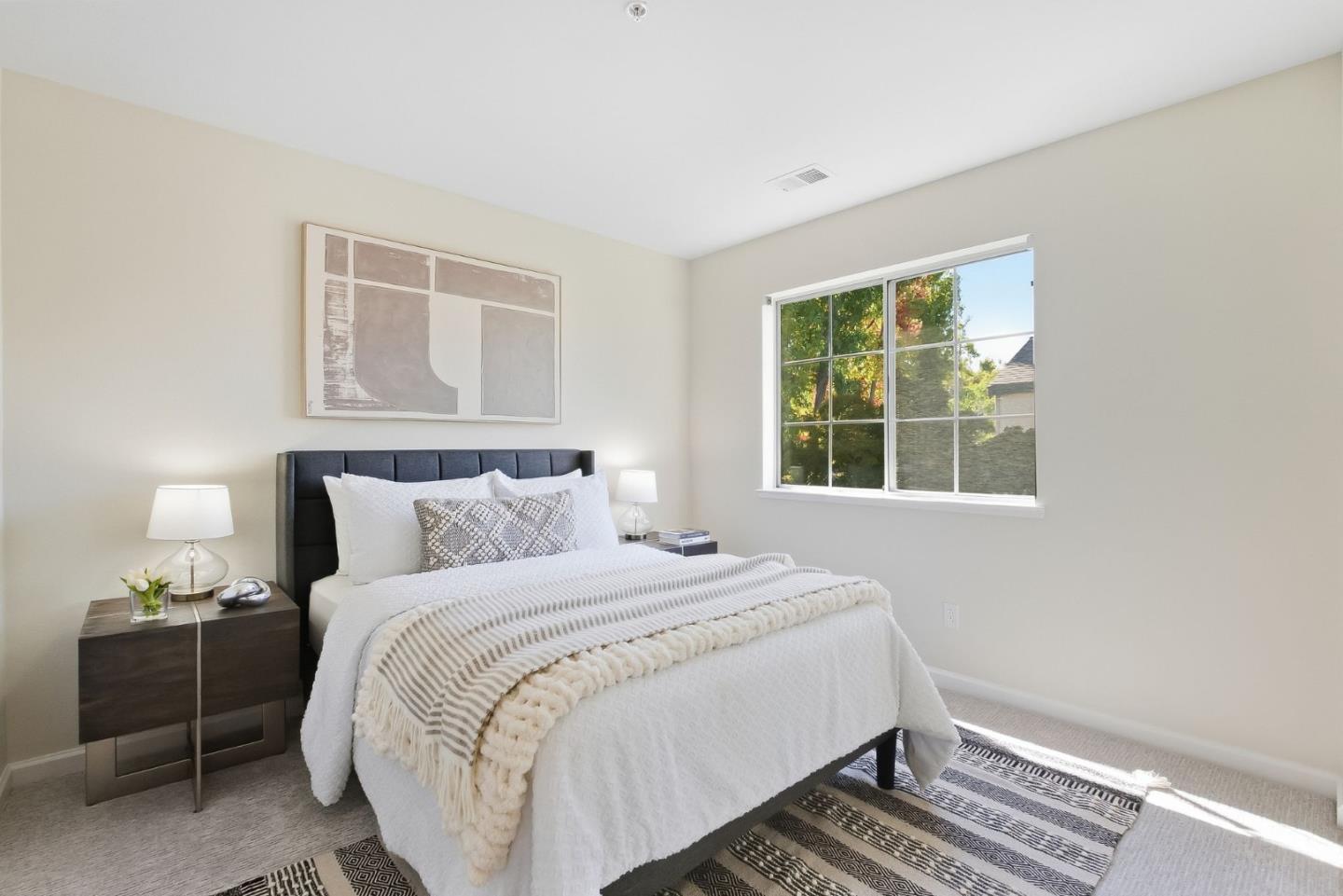 Staged bedroom with white bedding, framed abstract art, and a large window overlooking trees.