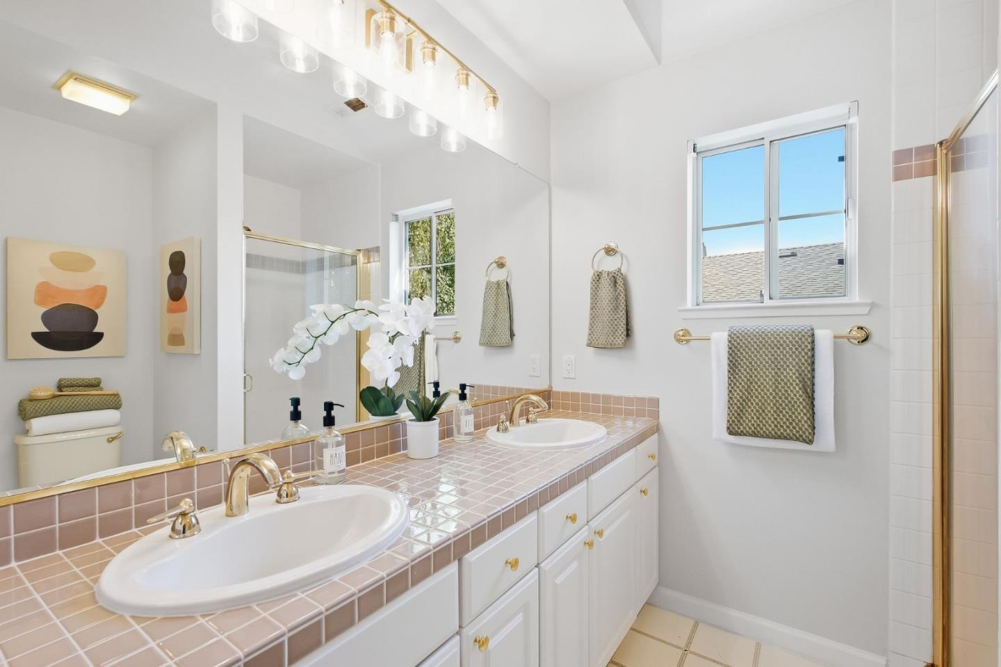 Bathroom with pink-tile double vanity, gold fixtures, large mirror, and glass shower.
