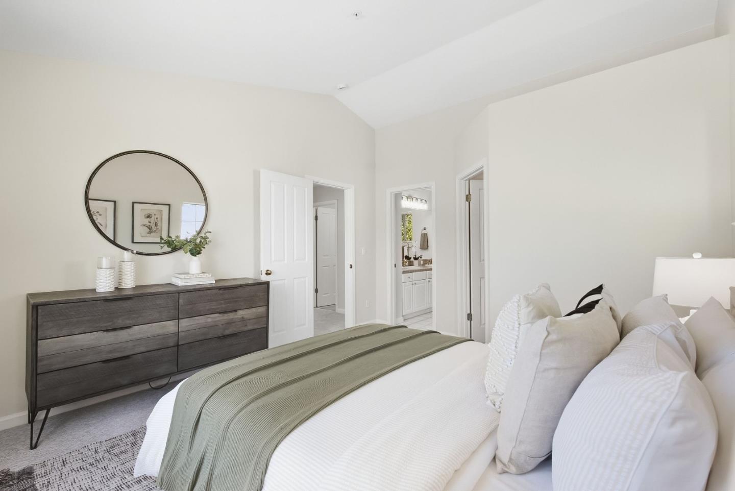 Staged bedroom with a sage-green bed throw, dark wood dresser, and large round mirror.