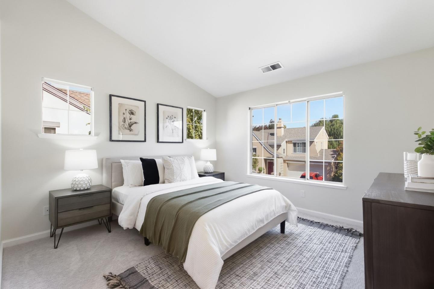 Staged bedroom with a large bed, framed botanical prints, and sunlit windows.