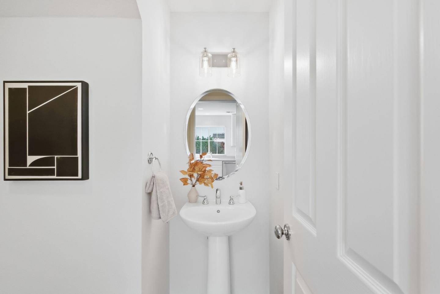 Bright bathroom with a pedestal sink, round mirror, and geometric wall art.