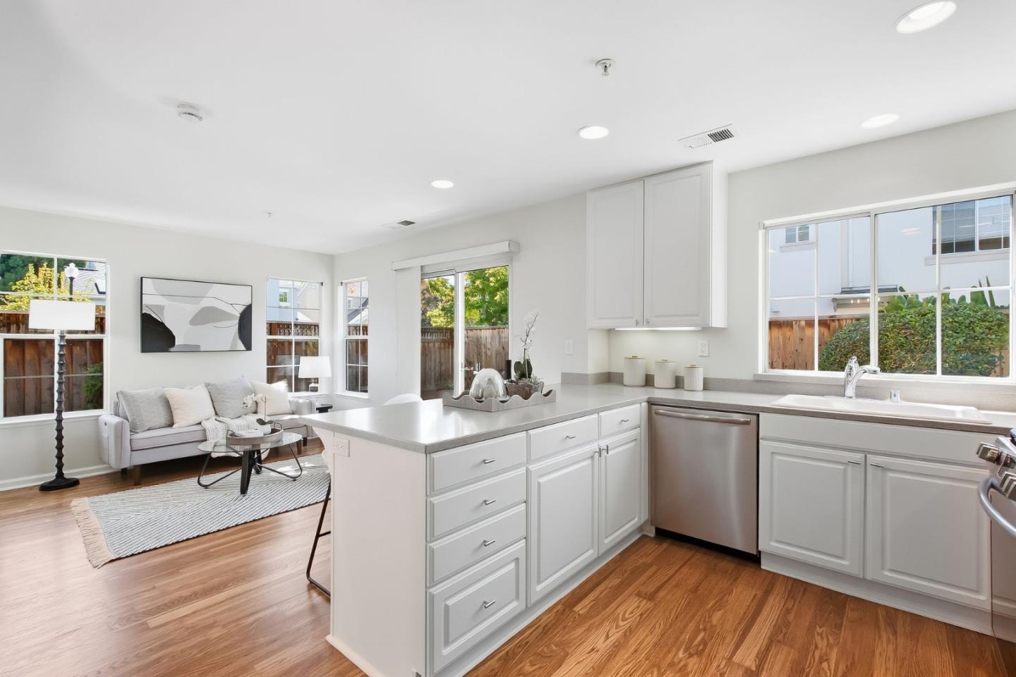 Bright white kitchen with a central island, stainless dishwasher, and adjoining sitting area.