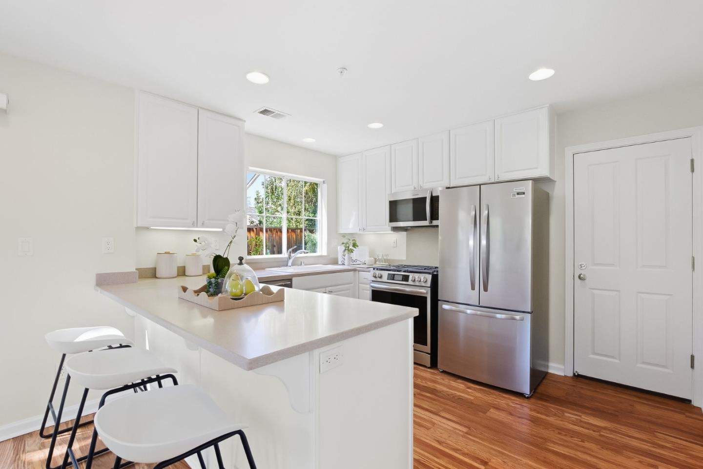 Bright white kitchen with a large peninsula, bar chairs, stainless steel appliances, and hardwood floors.