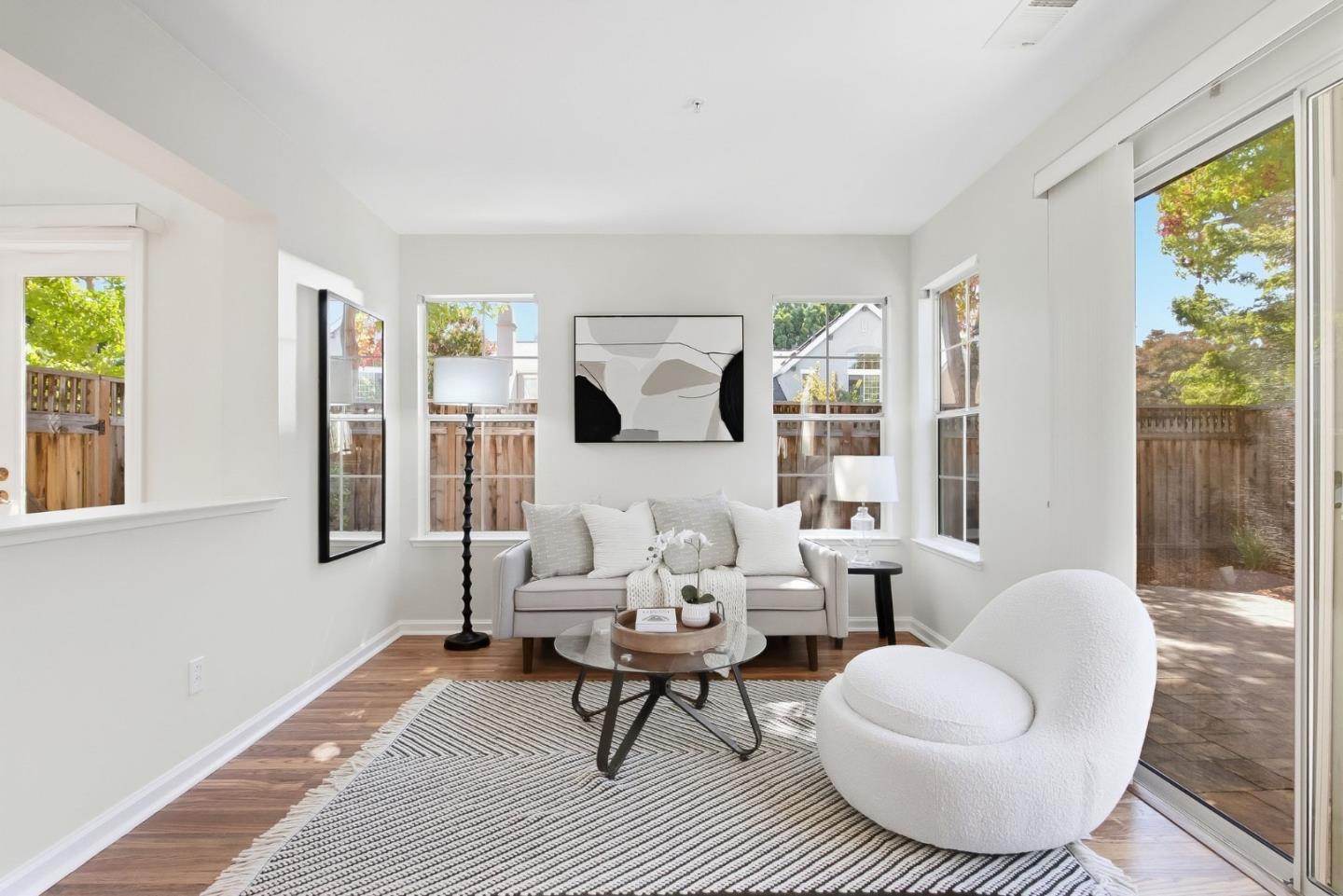 Bright living room with a gray sofa, rounded white chair, striped rug, and large backyard-facing windows.
