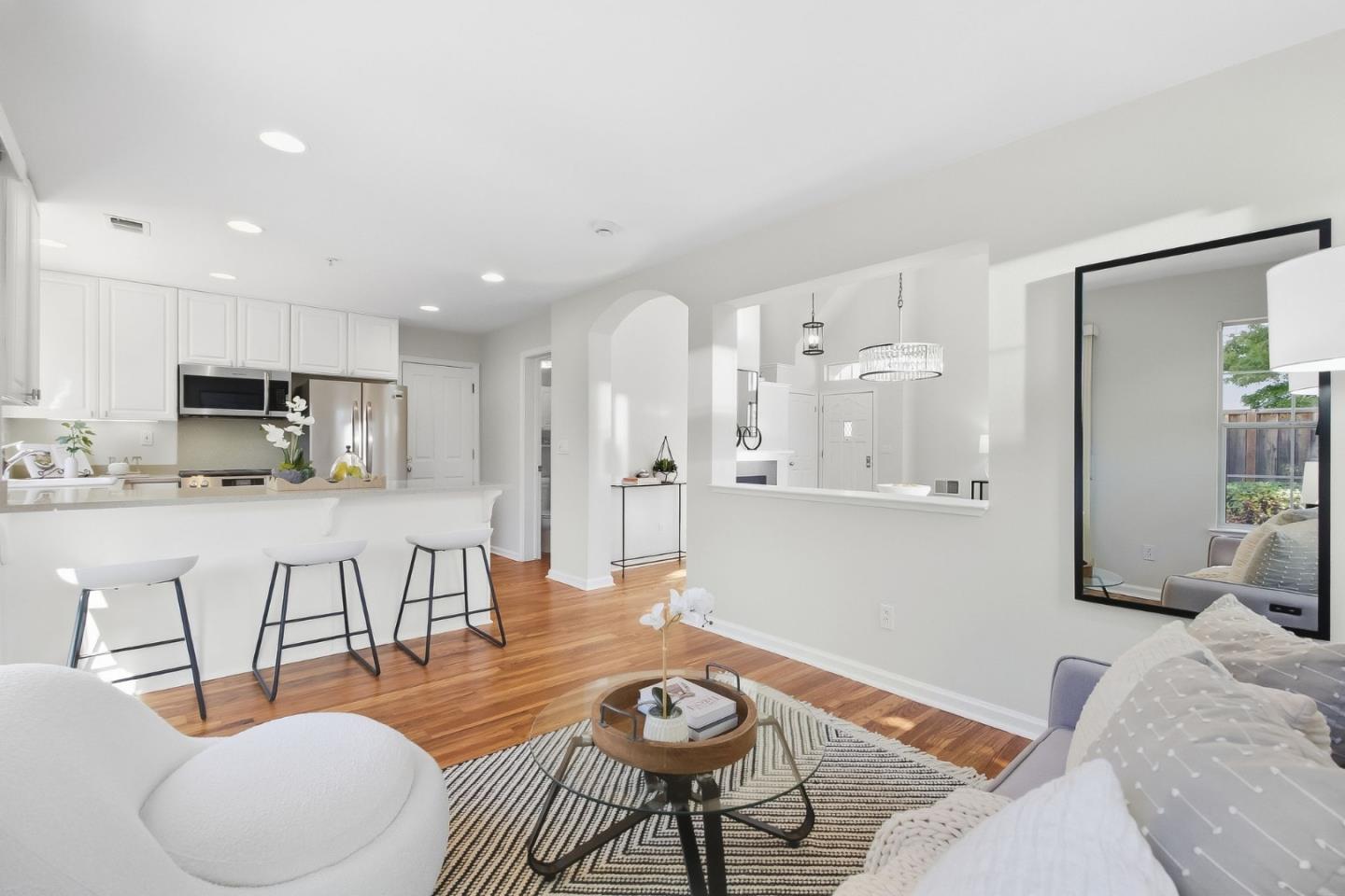 Open-plan kitchen and living room with white cabinetry, breakfast bar, and hardwood floors.