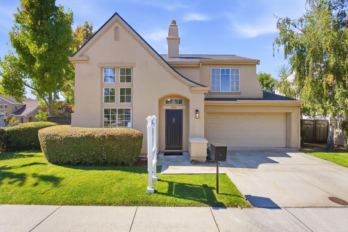 Two-story beige stucco home with an attached double garage and a neatly trimmed front lawn.
