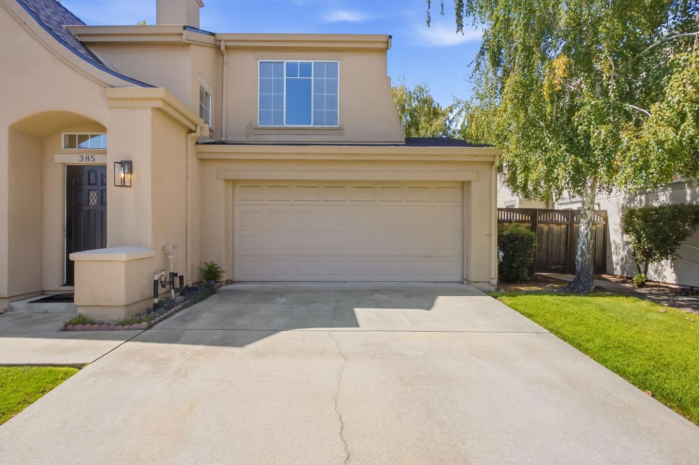 Two-story beige home with an arched entry and wide two-car garage.