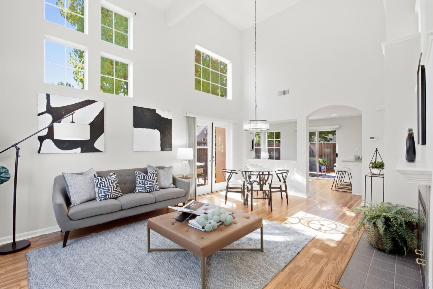 Staged living room with vaulted ceilings, tall windows, gray sofa, and adjoining dining area.
